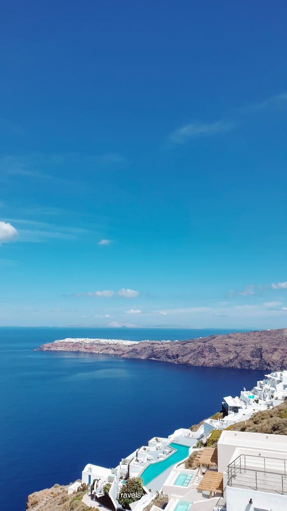 Image of Grace Hotel Imerovigli with a large infinity pool and in the background is the sea and cliffs of Santorini.
