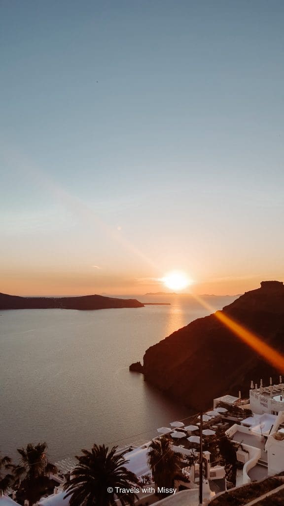Sunset in Imerovigli with a restaurant or hotel with umbrellas in the foreground.