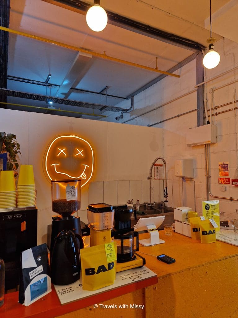 Inside Bad Coffee in Hackney Wick - pictured is an sign of a smiley face, bags of coffee beans on the counter and a coffee machine in a vibrant yellow colour.