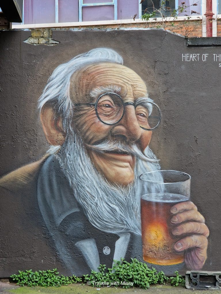 Grafitti artwork of an elderly man with white hair and a beard holding a beer in Hackney Wick
