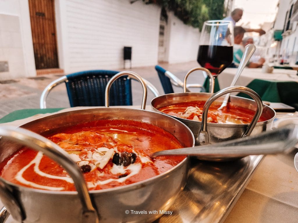 Two silver dishes with bright red butter chicken on a table in A Taste of India Nerja.
