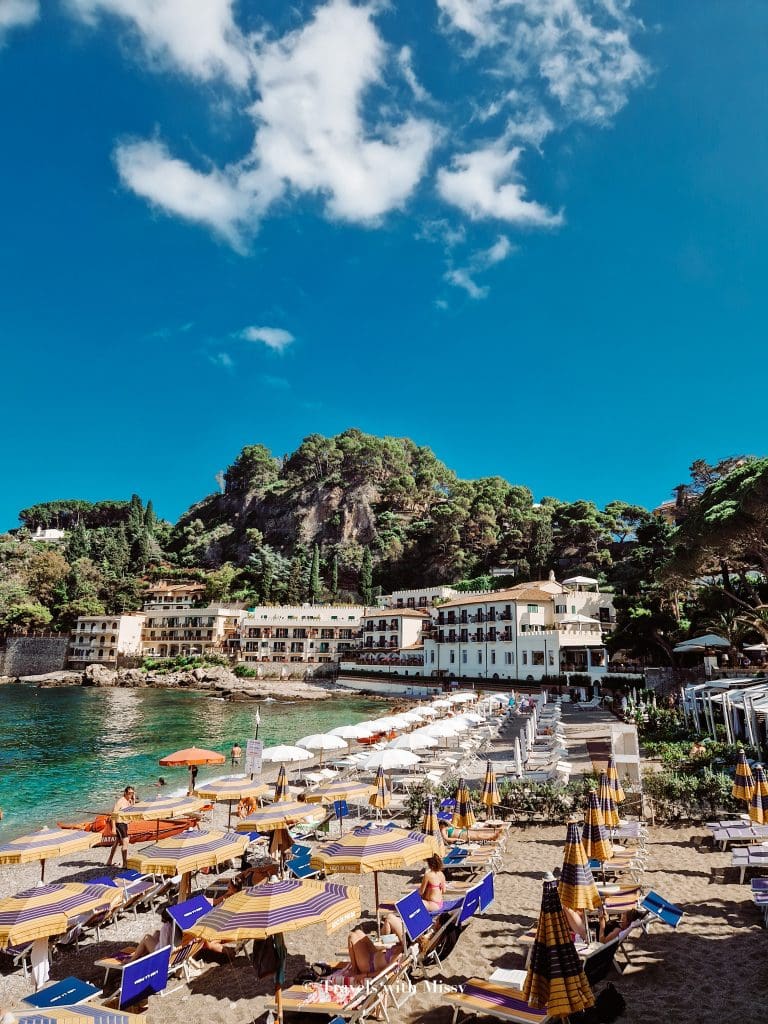 The coloured umbrellas and sun loungers of Mazzaro Beach in Taormina in the forefront of the picture. 