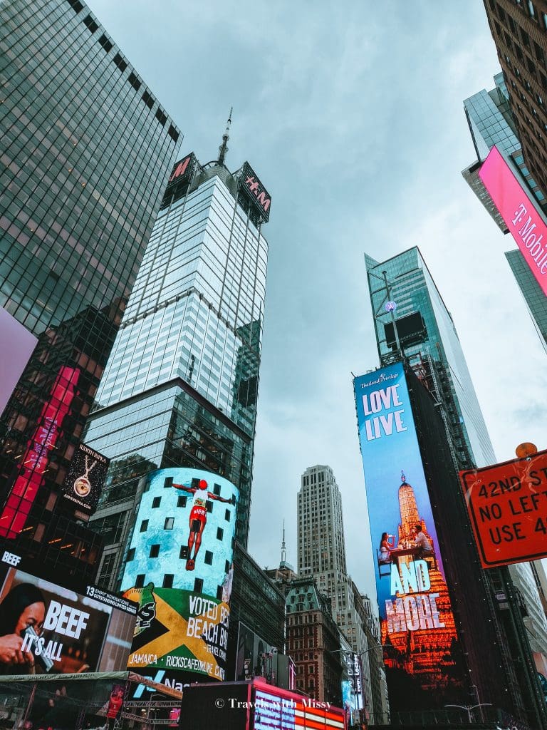 Time Square New York during the day is lit up with advertisements and lighting. 