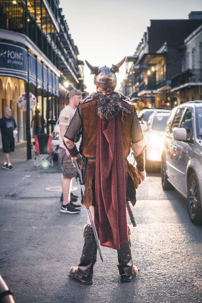 A man dressed in a Viking costume stands on a busy street with cars. 
